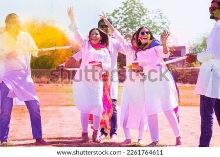 Group of happy young Indian people celebrating holi festival at park outdoor, Playful guys and girls with colorful paint faces playing with gulal.