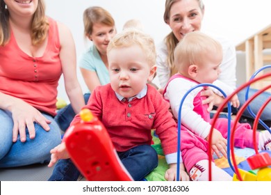 Group Of Happy Young Mothers Watching Their Cute And Healthy Babies While Playing With Multicolored Toys In A Modern Daycare Center