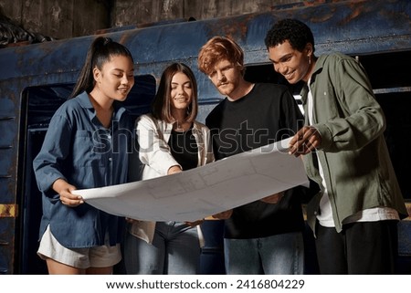 group of happy young multicultural friends solving quest task while looking at map in escape room