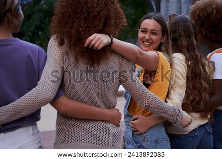 Group of happy young multiracial people embracing together outdoors. Five female friends seen from behind as one of them smiles at another. concept of empowered woman. Copy space.