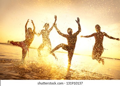 group of happy young people dancing and spraying at the beach on  beautiful summer sunset