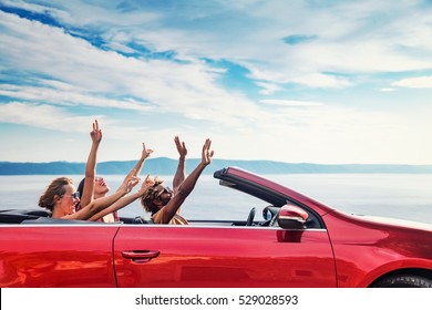 Group of happy young people raising hands to the air in the red convertible. - Powered by Shutterstock