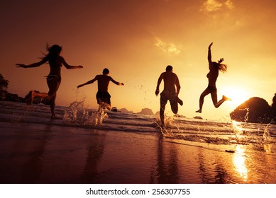 Group Of Happy Young People Is Running On Background Of Sunset Beach And Sea