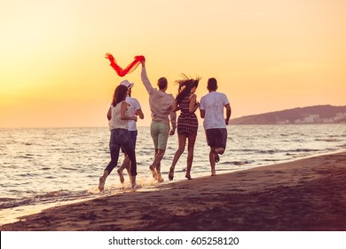 Group of happy young people is running on background of sunset beach and sea - Shutterstock ID 605258120