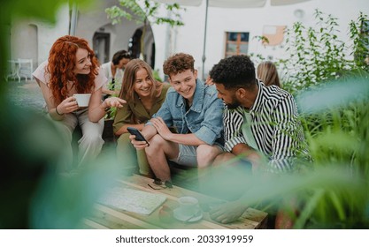 Group of happy young people with smartphone sitting in outdoors cafe on town trip, talking. - Powered by Shutterstock