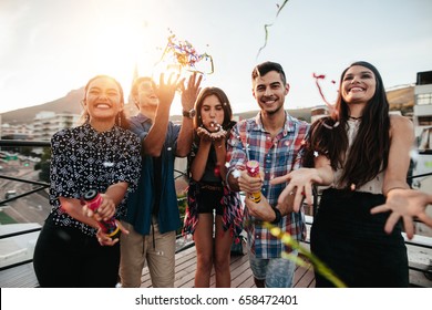 Group of happy young people throwing confetti while enjoying rooftop party. Friends having fun at terrace party.