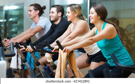 Group of happy young people training on exercise bikes in gym