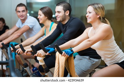 Group of happy young people training on exercise bikes in gym
