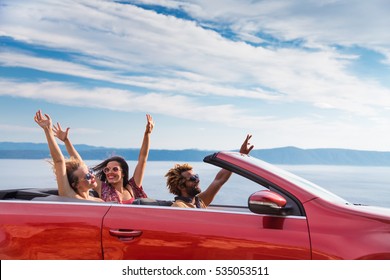 Group Of Happy Young People Waving From The Red Convertible.