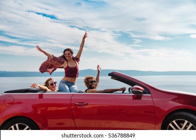 Group Of Happy Young People Waving From The Red Convertible.