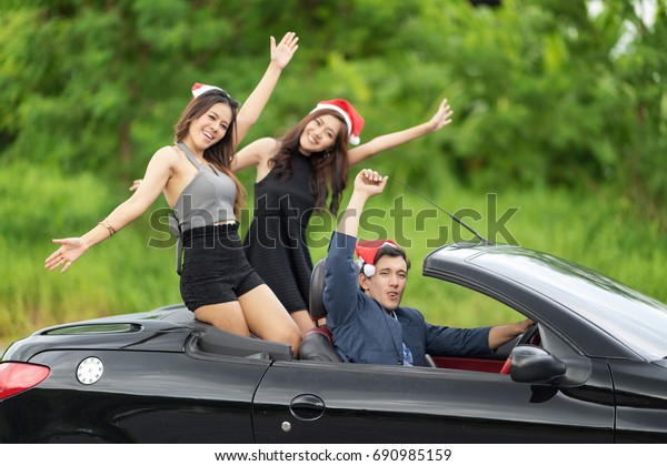 Group of happy young people wearing Santa hat and\
enjoying Christmas party on road trip in convertible car,\
celebrating with pink champagne.Concept of success businessman in\
Luxury life.