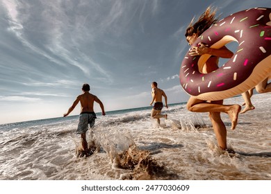 Group of happy young tourists runs and jumps with inflatable donuts at sea beach - Powered by Shutterstock