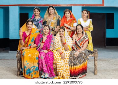 Group of happy young traditional indian women housewives wearing colorful sari sitting looking at camera with smile on face. Rural india. women empowerment.