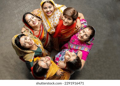 Group of happy young traditional indian women wearing colorful sari looking up and embracing each other like a team. Rural india. women empowerment. World women's day, Top view.