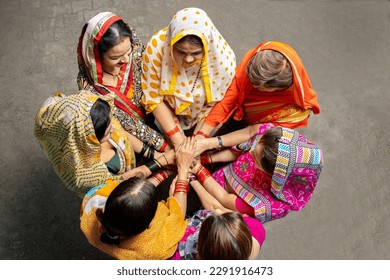 Group of happy young traditional indian women wearing colorful sari join hands with each other like a team. Rural india. women empowerment. Top view.