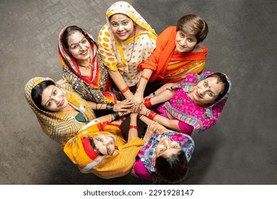 Group of happy young traditional indian women wearing colorful sari looking up while join hands with each other like a team. Rural india. women empowerment. World women's day, Top view