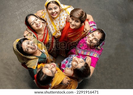 Group of happy young traditional indian women wearing colorful sari looking up and embracing each other like a team. Rural india. women empowerment. World women's day, Top view.