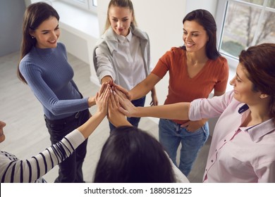 Group of happy young women standing in circle, putting hands together and smiling, feeling strong and united. Business team, aiming at success, reaching goal, unity, support, women's rights concepts