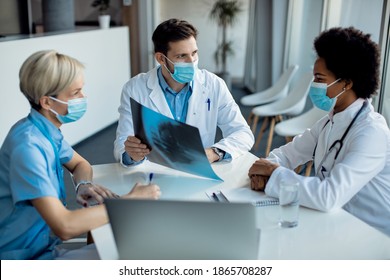 Group of healthcare experts wearing face masks and analyzing X-ray image during a meeting at medical clinic. Focus is on male doctor.  - Powered by Shutterstock