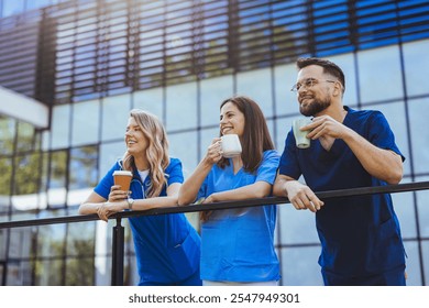 A group of healthcare professionals in scrubs enjoying a sunny coffee break outside a modern building, showcasing teamwork and relaxation. Smiling and holding cups, they exude a positive work  - Powered by Shutterstock