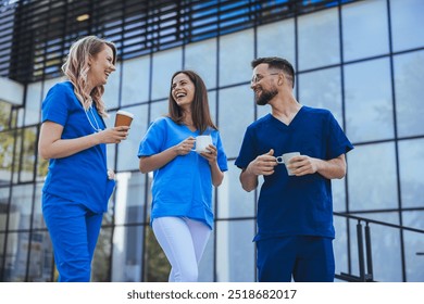 A group of healthcare professionals in uniforms smiling and talking while enjoying a coffee break outside a modern hospital building. - Powered by Shutterstock