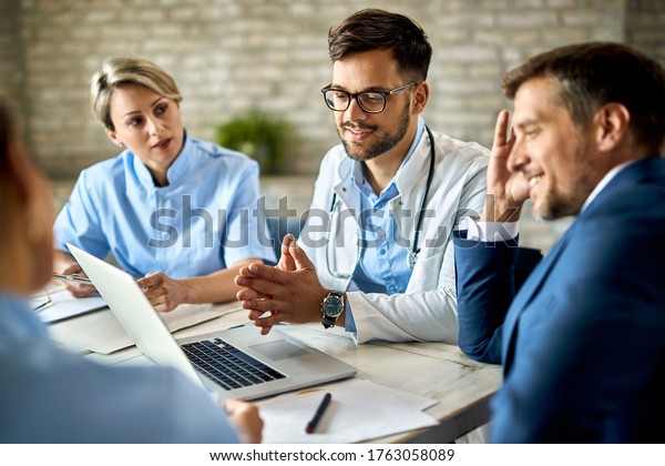 Group\
of healthcare workers and businessman using laptop while having a\
meeting in the office. Focus is on young doctor.\
