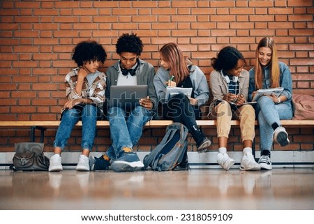 Group of high school friends cooperating while studying in hallway at school. Copy space.