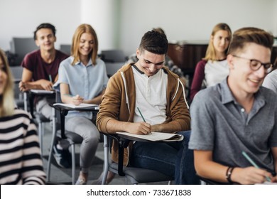 Group of high school students sitting in classroom and writing in notebooks.