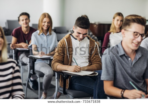 Group of high school students sitting in\
classroom and writing in\
notebooks.