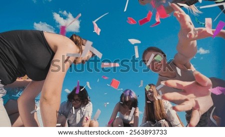 Group of high school students throwing colorful confetti in the air, celebrating the end of school year under a bright summer sky