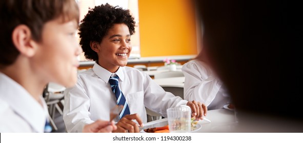 Group Of High School Students Wearing Uniform Sitting Around Table And Eating Lunch In Cafeteria