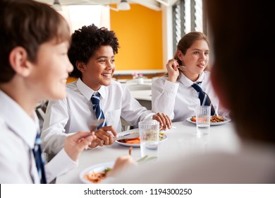 Group Of High School Students Wearing Uniform Sitting Around Table And Eating Lunch In Cafeteria