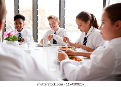 Group Of High School Students Wearing Uniform Sitting Around Table And Eating Lunch In Cafeteria