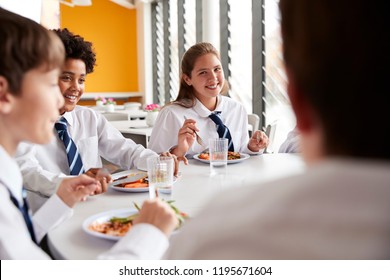 Group Of High School Students Wearing Uniform Sitting Around Table And Eating Lunch In Cafeteria