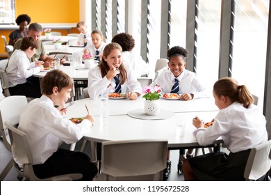 Group Of High School Students Wearing Uniform Sitting Around Table And Eating Lunch In Cafeteria