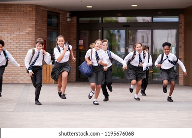 Group Of High School Students Wearing Uniform Running Out Of School Buildings Towards Camera At The End Of Class