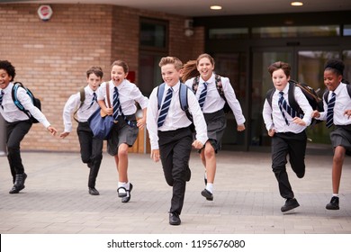 Group Of High School Students Wearing Uniform Running Out Of School Buildings Towards Camera At The End Of Class