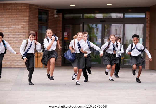 Group Of\
High School Students Wearing Uniform Running Out Of School\
Buildings Towards Camera At The End Of\
Class