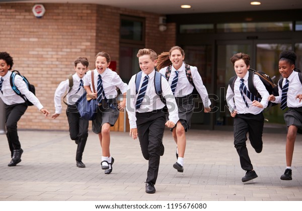 Group Of\
High School Students Wearing Uniform Running Out Of School\
Buildings Towards Camera At The End Of\
Class