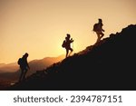 Group of hikers with backpacks walks uphill in sunset mountains