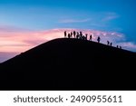 A group of hikers silhouetted against a vibrant sunset sky on a volcanic peak. The scene captures the sense of adventure and the breathtaking beauty of high-altitude landscapes.