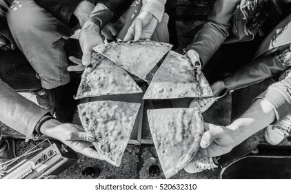 Group of hipster friends toasting pizza take away on staircase city center - Top view of young people sharing food and time together - Black and white editing - Focus on  pizza slices