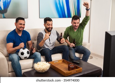 Group Of Hispanic Male Friends Watching A Soccer Game On TV And Drinking Some Beer