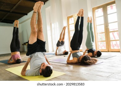 Group of hispanic people doing yoga in a studio. Active women and men exercising while practicing a shoulder stand inversion