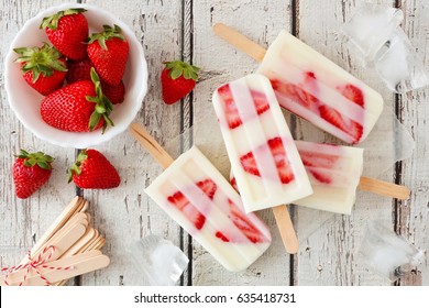 Group of homemade strawberry vanilla popsicles on a rustic white wood background