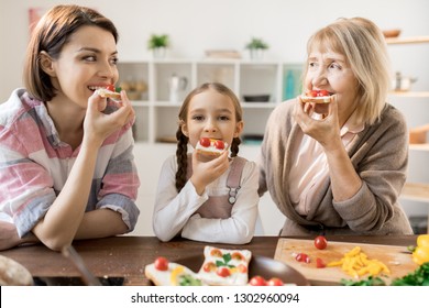 Group Of Hungry Females Eating Homemade Sandwiches With Cheese And Cherry Tomatoes In The Kitchen