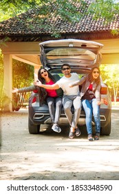 Group of Indian Asian young and attractive friends sitting in the open trunk of a car, a summer road trip