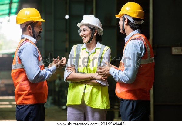 Group of Indian engineers wearing helmet and\
vest discussing and laughing, candid moment, Industrial factory\
concept, male and female worker smiling chatting in free time at\
project. work culture. 