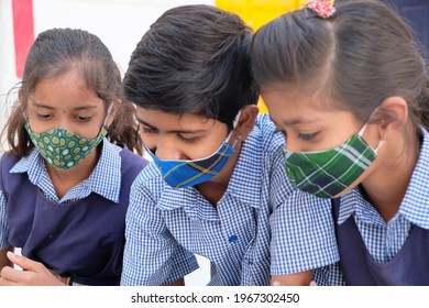 A Group Of Indian School Children In Face Masks And Uniforms Using A Tablet At School During Covid-19