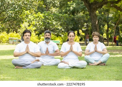 Group of indian senior people doing yoga sitting on grass. Mature man and woman wearing white cloths practicing meditation together outdoor. - Powered by Shutterstock